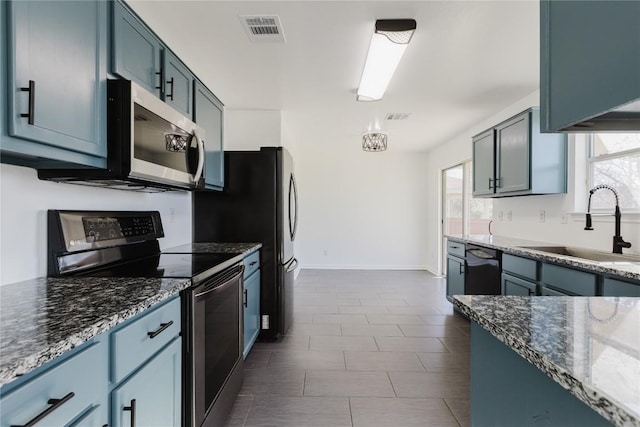 kitchen with blue cabinetry, appliances with stainless steel finishes, sink, and dark stone counters