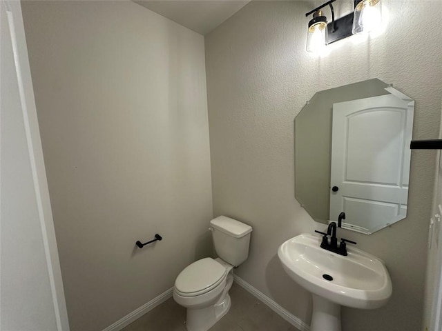 half bath with toilet, baseboards, and a sink