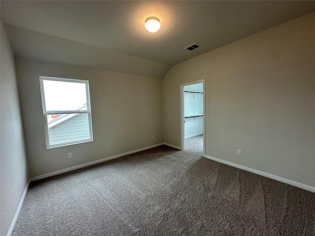 unfurnished room with visible vents, carpet floors, baseboards, and vaulted ceiling