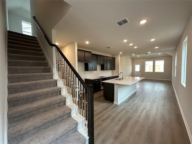 kitchen with a center island with sink, visible vents, decorative backsplash, light countertops, and light wood-style floors