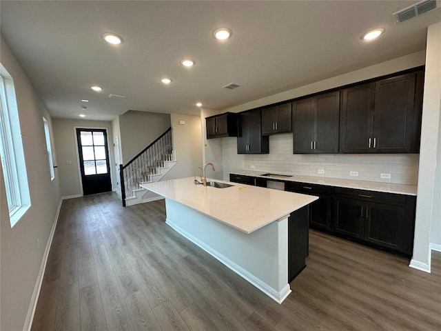 kitchen featuring wood finished floors, visible vents, a kitchen island with sink, a sink, and decorative backsplash