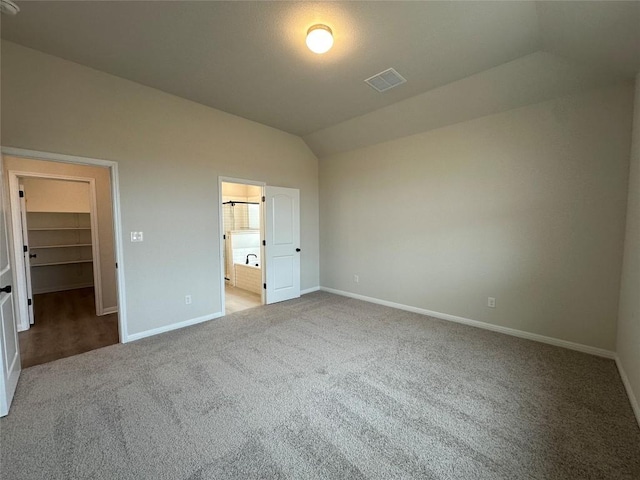 unfurnished bedroom featuring carpet, visible vents, baseboards, vaulted ceiling, and a spacious closet