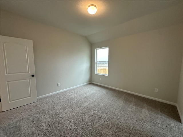 carpeted spare room featuring lofted ceiling and baseboards