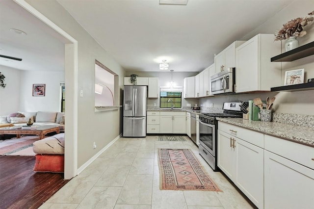 kitchen with pendant lighting, sink, stainless steel appliances, light stone counters, and white cabinets