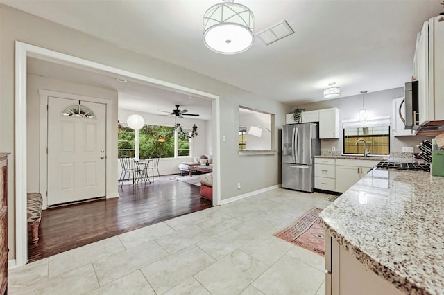 kitchen with light tile patterned floors, appliances with stainless steel finishes, white cabinetry, hanging light fixtures, and light stone counters