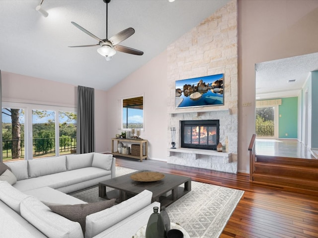 living room featuring a stone fireplace, hardwood / wood-style floors, high vaulted ceiling, ceiling fan, and a textured ceiling