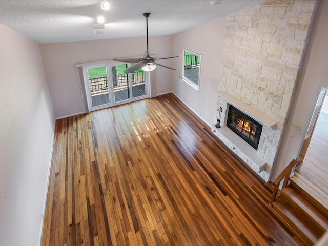 unfurnished living room featuring ceiling fan, a stone fireplace, lofted ceiling, and dark hardwood / wood-style flooring