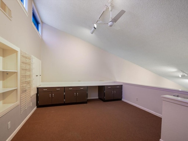 unfurnished office featuring ceiling fan, lofted ceiling, dark carpet, and a textured ceiling