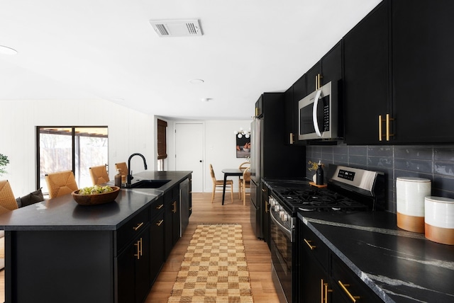 kitchen featuring sink, light hardwood / wood-style flooring, stainless steel appliances, tasteful backsplash, and a center island with sink