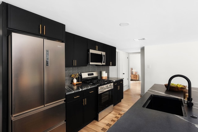 kitchen with tasteful backsplash, appliances with stainless steel finishes, sink, and light hardwood / wood-style floors