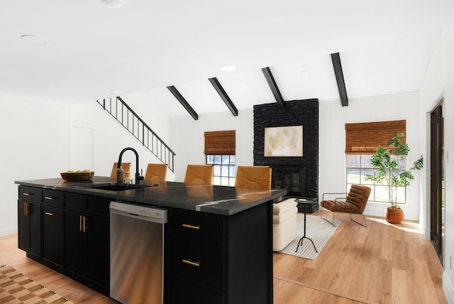 kitchen with sink, dishwasher, a kitchen island with sink, a fireplace, and light hardwood / wood-style floors