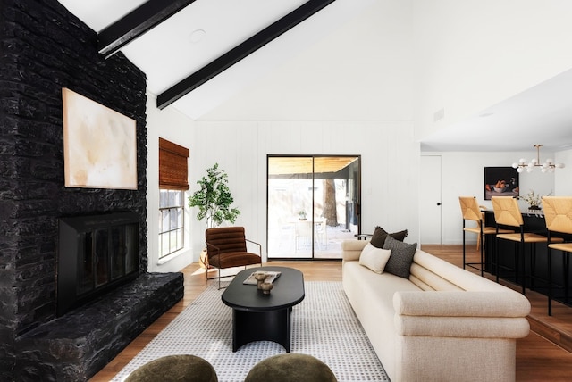 living room featuring vaulted ceiling with beams, a stone fireplace, wood-type flooring, and a chandelier