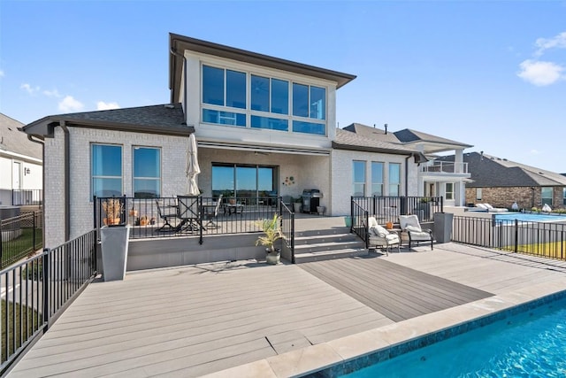 back of house featuring a deck, a patio, brick siding, and a fenced in pool