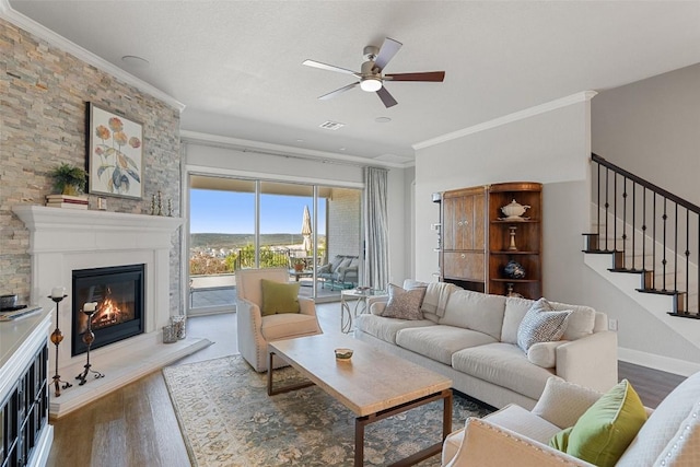 living area featuring stairs, a glass covered fireplace, ornamental molding, and wood finished floors