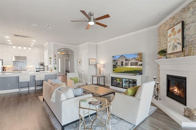 living room featuring visible vents, arched walkways, a glass covered fireplace, dark wood-style floors, and ornamental molding