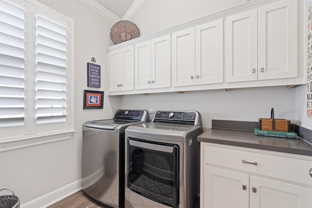 laundry room featuring cabinet space, baseboards, wood finished floors, washing machine and clothes dryer, and crown molding