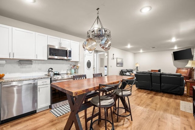 kitchen featuring tasteful backsplash, light stone counters, light hardwood / wood-style flooring, appliances with stainless steel finishes, and white cabinets