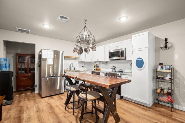 kitchen with white cabinetry, decorative backsplash, appliances with stainless steel finishes, and hanging light fixtures