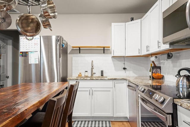 kitchen featuring appliances with stainless steel finishes, tasteful backsplash, sink, white cabinets, and light stone countertops