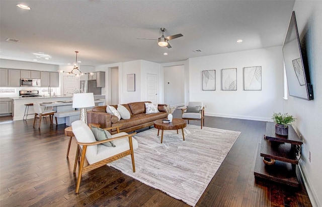 living room with dark wood-type flooring, ceiling fan with notable chandelier, and a textured ceiling