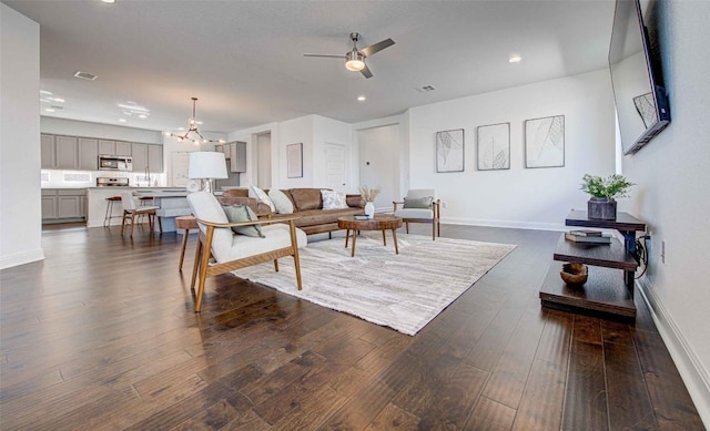 living room with dark hardwood / wood-style flooring and ceiling fan with notable chandelier