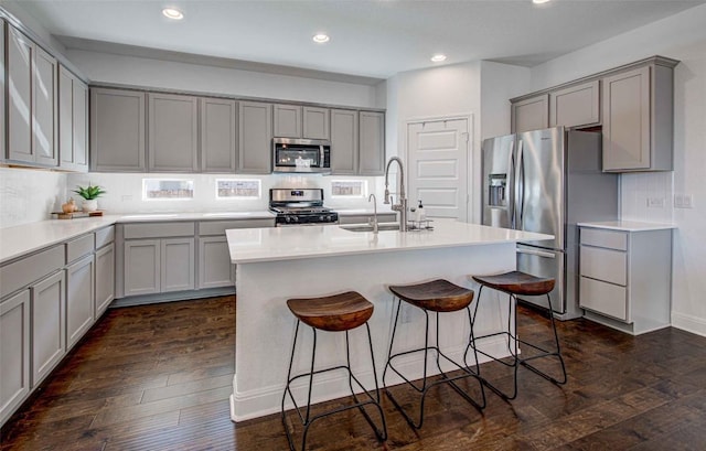 kitchen featuring sink, gray cabinets, appliances with stainless steel finishes, a kitchen island with sink, and dark hardwood / wood-style flooring