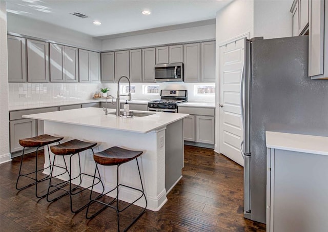 kitchen with sink, a kitchen breakfast bar, stainless steel appliances, dark hardwood / wood-style floors, and a center island with sink