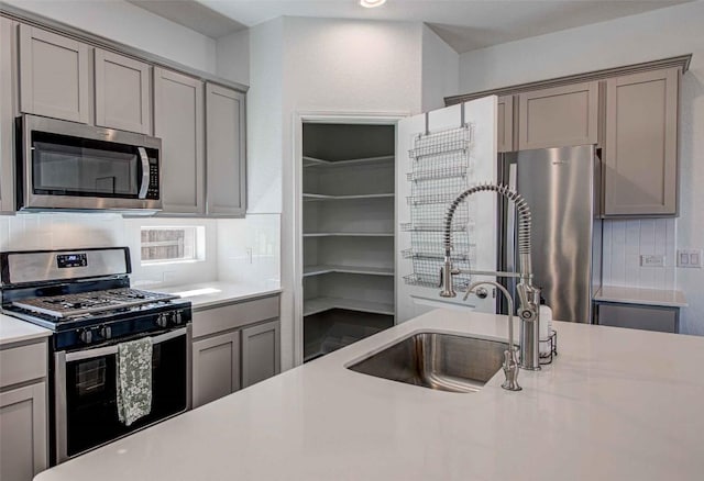 kitchen with gray cabinetry, appliances with stainless steel finishes, sink, and backsplash