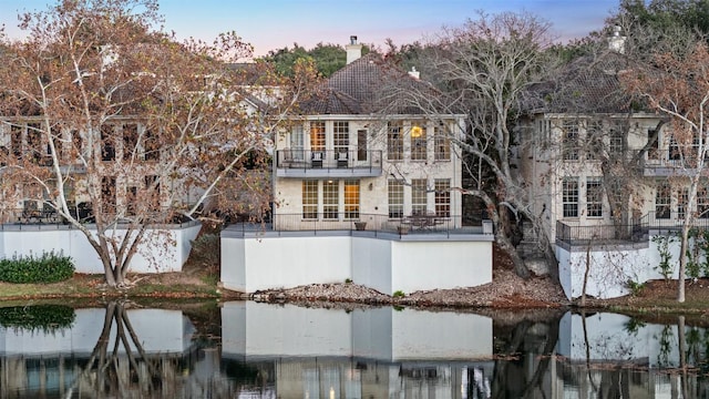 back house at dusk with a balcony and a water view