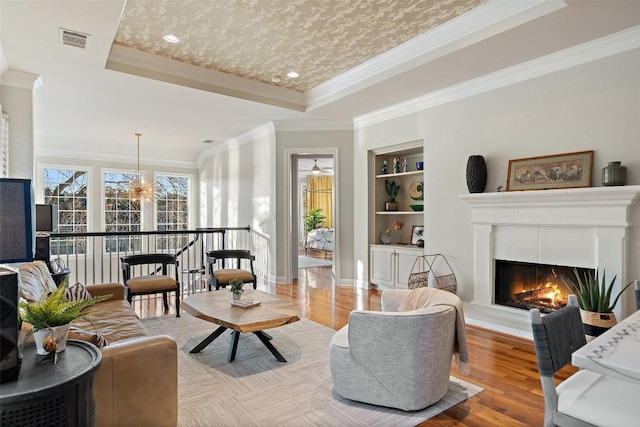 living room featuring a raised ceiling, ornamental molding, built in features, and light hardwood / wood-style floors