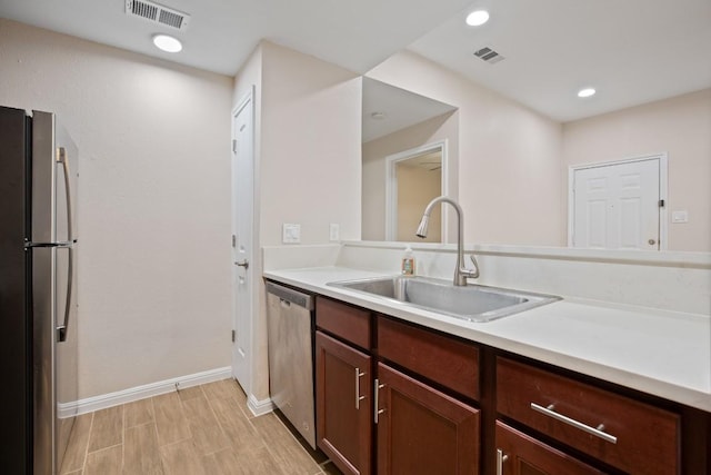 kitchen with stainless steel appliances, dark brown cabinets, sink, and light hardwood / wood-style floors