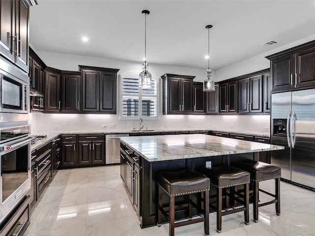 kitchen featuring a kitchen island, appliances with stainless steel finishes, decorative light fixtures, tasteful backsplash, and a breakfast bar area