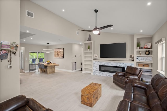 living area with visible vents, built in features, a glass covered fireplace, ceiling fan, and light wood-type flooring