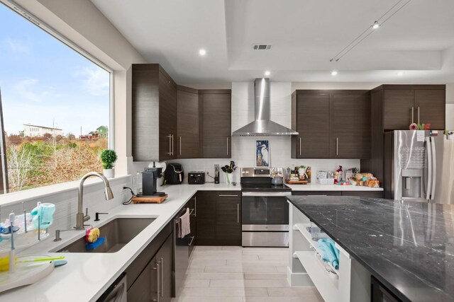 kitchen with appliances with stainless steel finishes, sink, dark brown cabinets, and wall chimney range hood