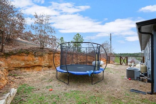 view of yard featuring a trampoline, fence, and central AC unit