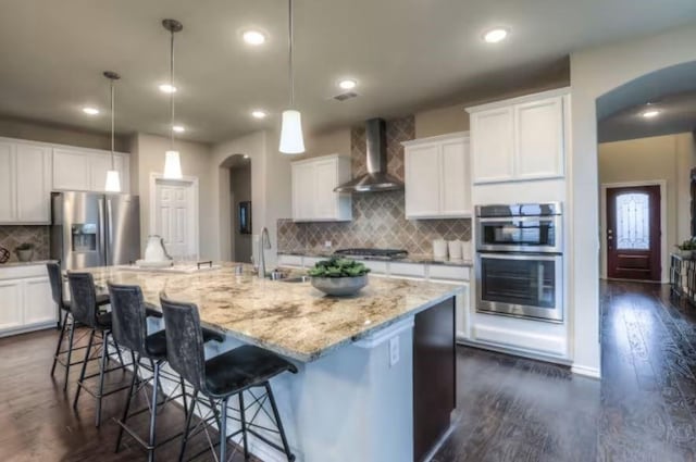 kitchen featuring a kitchen island with sink, wall chimney range hood, hanging light fixtures, and sink