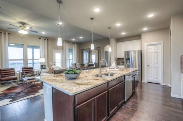 kitchen with pendant lighting, sink, appliances with stainless steel finishes, dark hardwood / wood-style floors, and a center island with sink