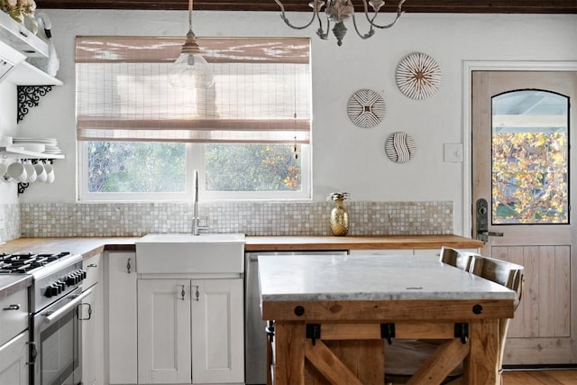 kitchen featuring white cabinetry, sink, backsplash, high end stainless steel range oven, and hanging light fixtures