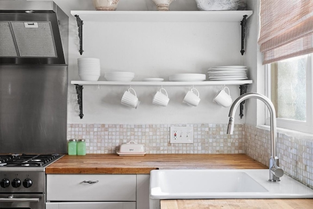 kitchen with decorative backsplash, sink, wooden counters, and stainless steel gas stove