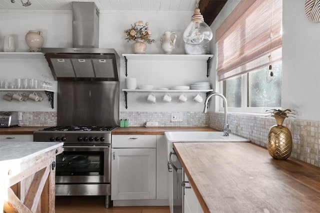 kitchen featuring butcher block counters, hanging light fixtures, white cabinets, high end stove, and backsplash