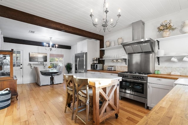 kitchen with wall chimney range hood, butcher block counters, stainless steel appliances, white cabinets, and a chandelier