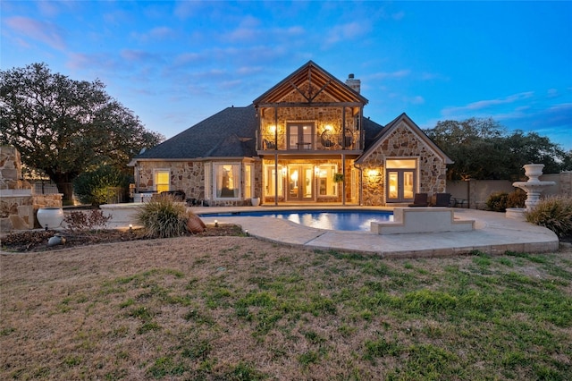 back house at dusk featuring french doors, a balcony, and a patio area