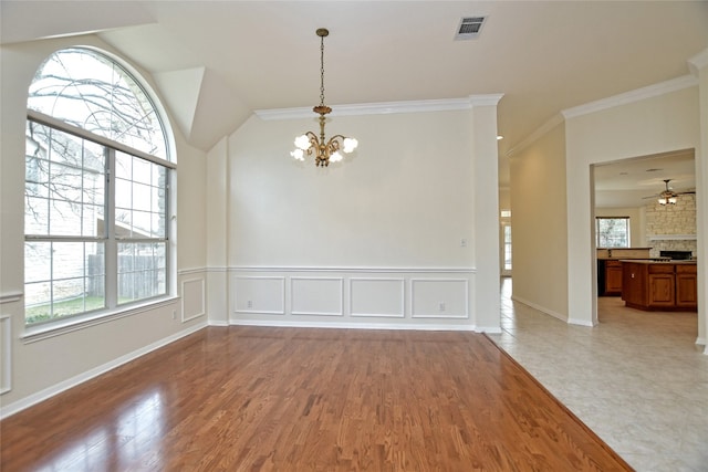 unfurnished dining area featuring ornamental molding, a stone fireplace, ceiling fan with notable chandelier, and light hardwood / wood-style floors