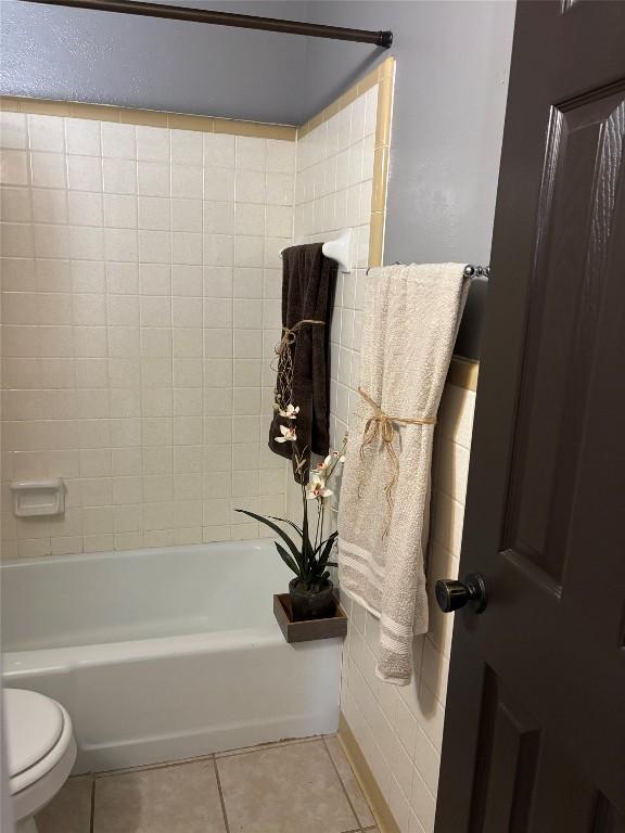 bathroom with tiled shower / bath combo, tile patterned floors, and toilet