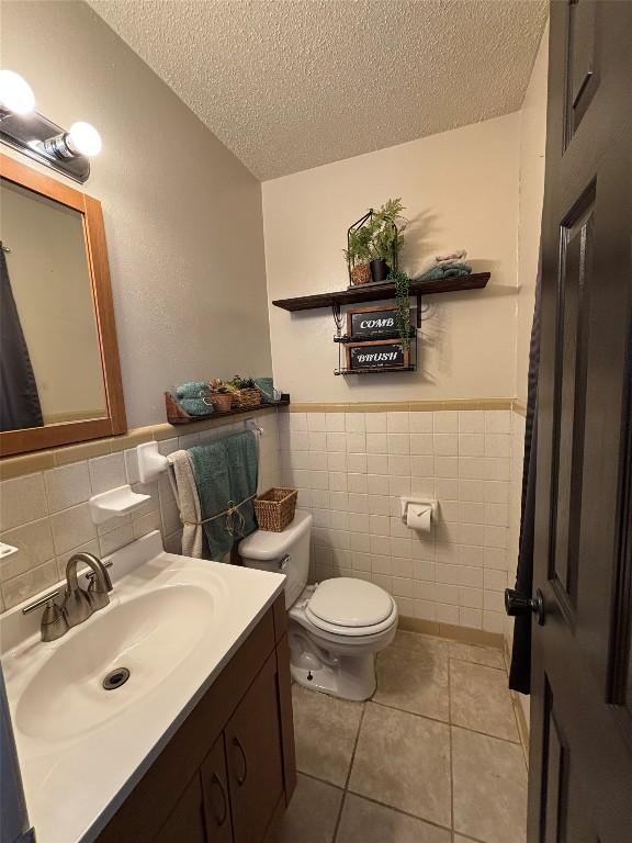 bathroom featuring tile walls, vanity, toilet, tile patterned floors, and a textured ceiling