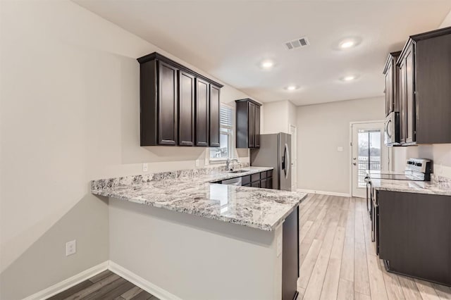 kitchen featuring appliances with stainless steel finishes, dark brown cabinets, light stone counters, kitchen peninsula, and light wood-type flooring