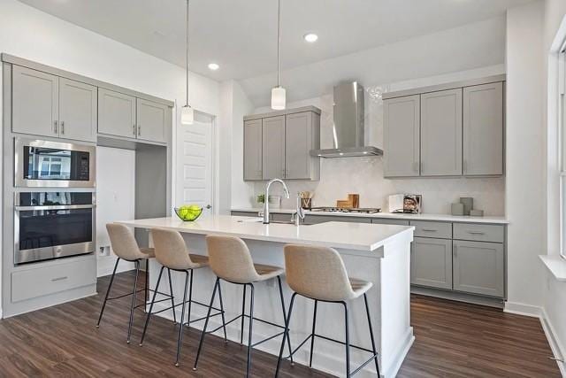 kitchen featuring wall chimney exhaust hood, sink, hanging light fixtures, a center island with sink, and stainless steel appliances