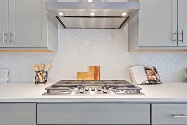 kitchen featuring gray cabinetry, tasteful backsplash, exhaust hood, and stainless steel gas cooktop