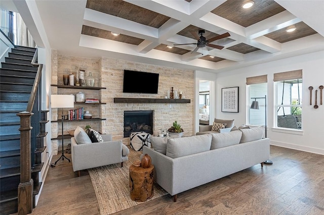 living room with a stone fireplace, dark hardwood / wood-style floors, coffered ceiling, ceiling fan, and beam ceiling