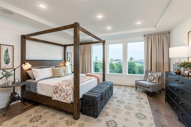 bedroom featuring a raised ceiling, dark hardwood / wood-style floors, and wood walls